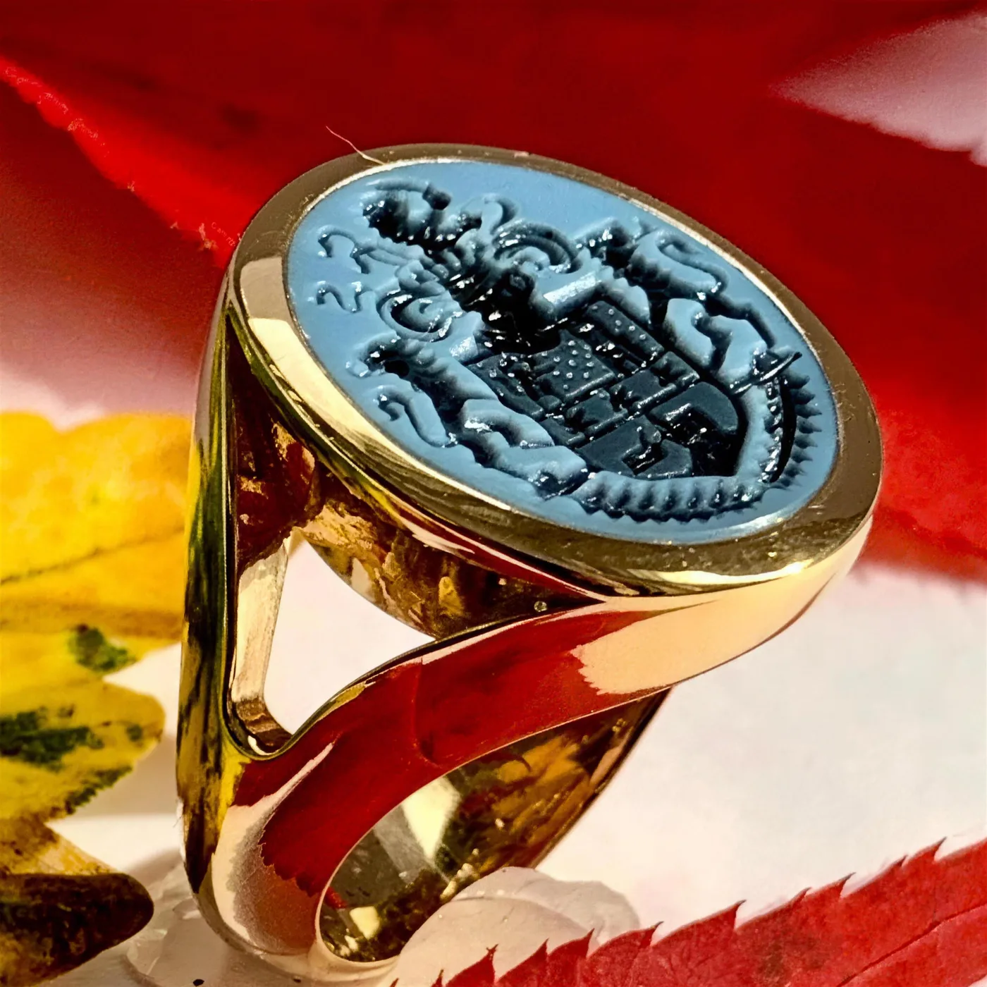 Goldener Siegelring mit fein graviertem Wappen auf hellblauem Lagenstein